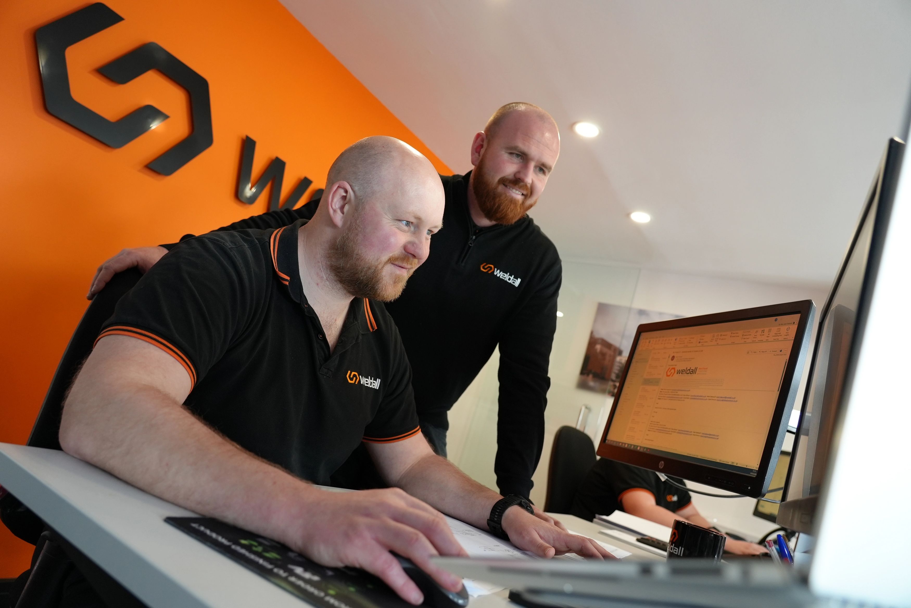 Two Weldall colleagues working together at a desktop computer in a modern office.