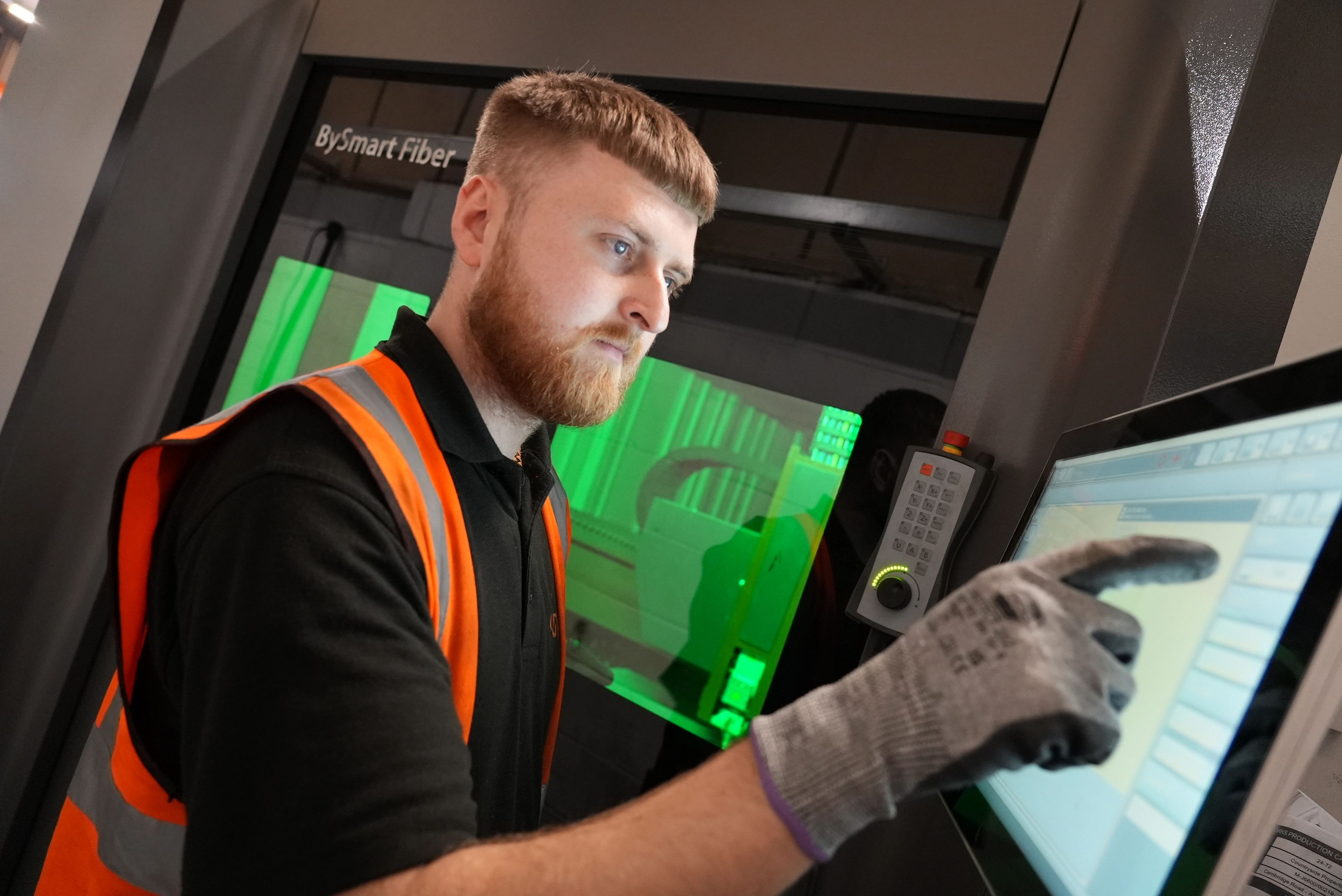 Weldall operator wearing a high-visibility vest and gloves using the control screen of a fiber laser machine.