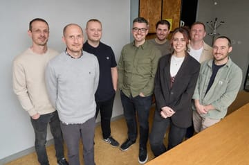 Tom, Jamie, Ryan, Nick, Emma, Andy, Lee and Jacob standing together for a team photo in a modern office.